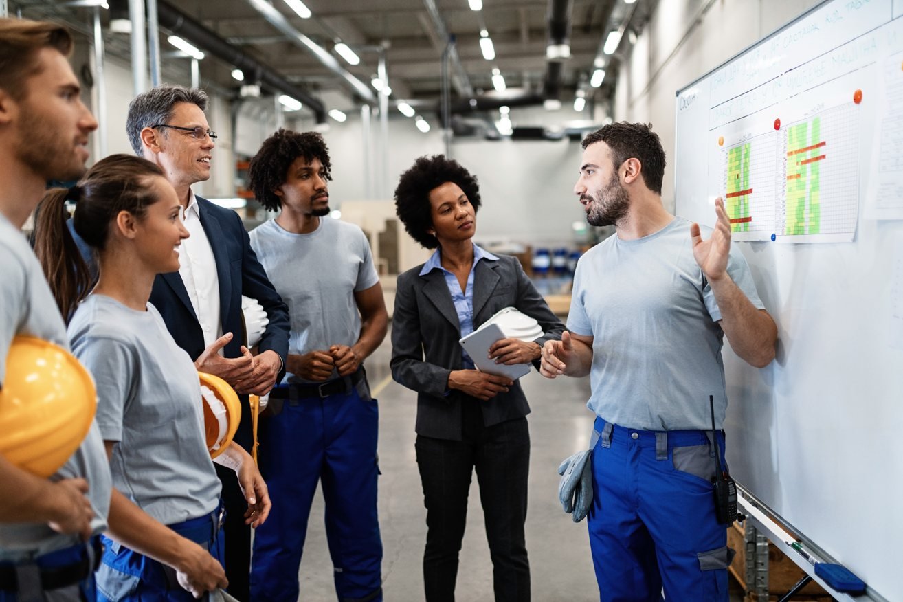 Instrutor explicando procedimentos de segurança para uma turma em um galpão industrial